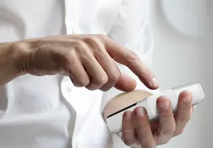 Eine Person hält ein medizinisches Gerät in der Hand und bedient es mit dem Finger. Das Bild zeigt eine Nahaufnahme der Hände vor hellem Hintergrund.