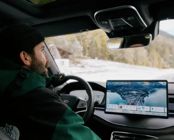 Ein Mann sitzt im Fahrersitz eines BYD Tang und blickt nach vorne. Im Innenraum ist das moderne Cockpit zu sehen, einschließlich des großen zentralen Touchscreens, der eine Navigationsansicht mit einer Karte anzeigt.