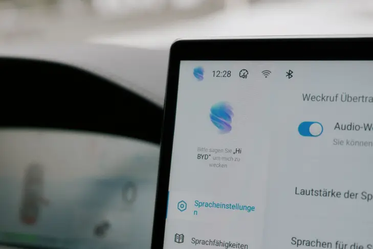 Nahaufnahme des zentralen Touchscreens im Innenraum eines BYD Tang. Der Bildschirm zeigt die Einstellungen für die Sprachsteuerung, unter anderem mit der Aufforderung: „Bitte sagen Sie ‚Hi BYD‘, um mich zu wecken.“ Rechts ist ein Schalter für „Audio-Weckruf“ sichtbar.