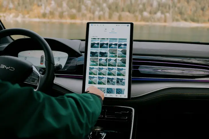 Innenansicht eines BYD Tang mit Fokus auf den großen zentralen Touchscreen im Cockpit. Der Bildschirm zeigt eine Galerieansicht mit mehreren Miniaturbildern von Landschaftsaufnahmen.