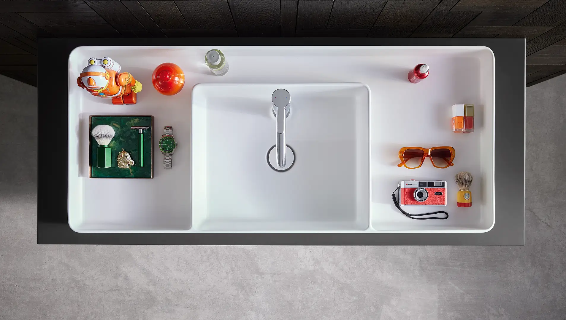 Weißes Waschbecken von Duravit mit integrierter Ablagefläche, die mit bunten Accessoires wie einer Kamera, Sonnenbrille und Pflegeprodukten dekoriert ist.
