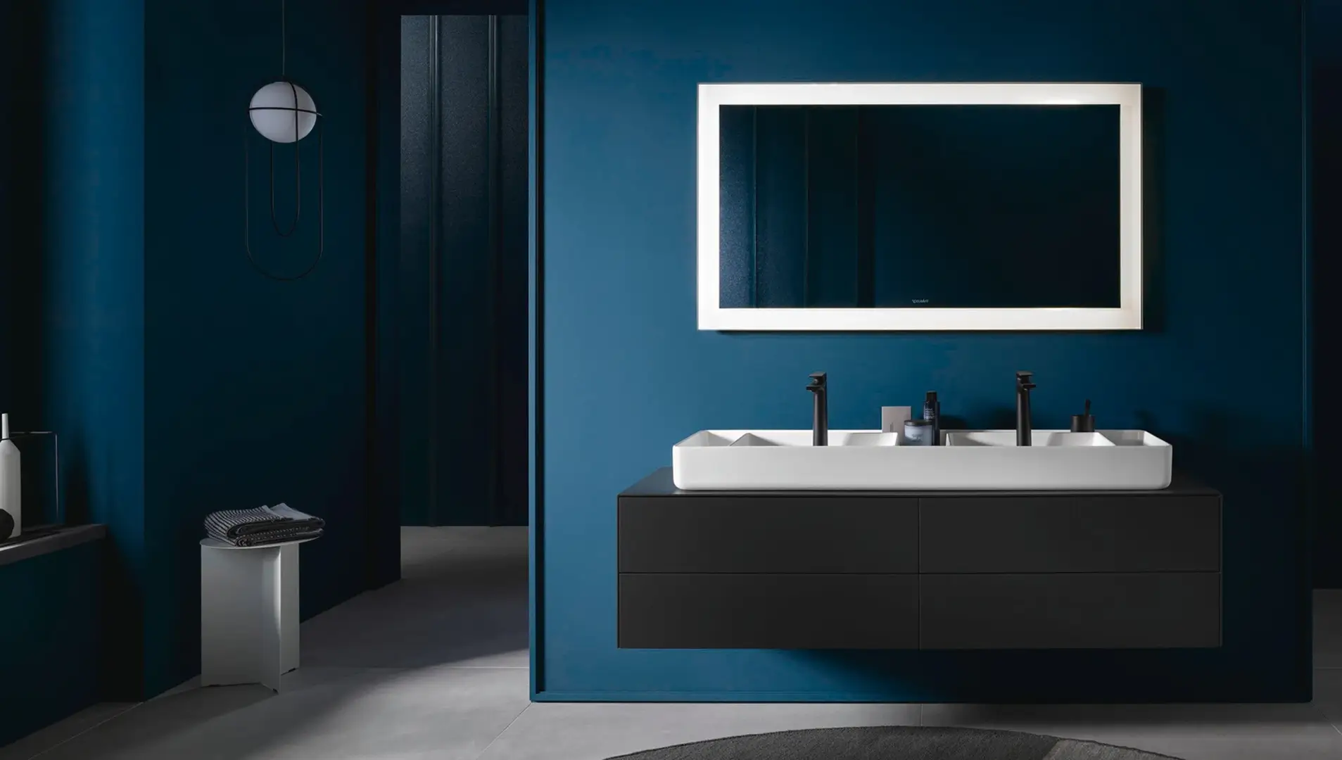 Modernes Badezimmer mit Doppelwaschbecken, beleuchtetem Spiegel und minimalistischer schwarzer Einrichtung.