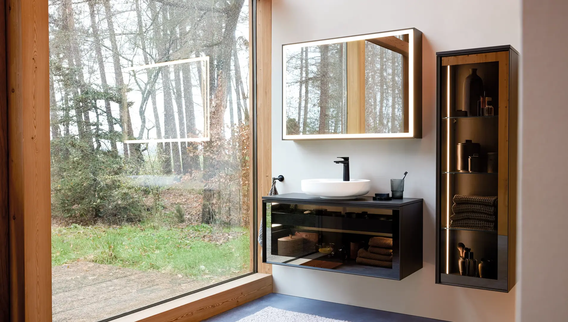Ein Badezimmer mit einem Duravit-Waschbecken und großem Fenster, das den Blick auf einen Wald freigibt.
