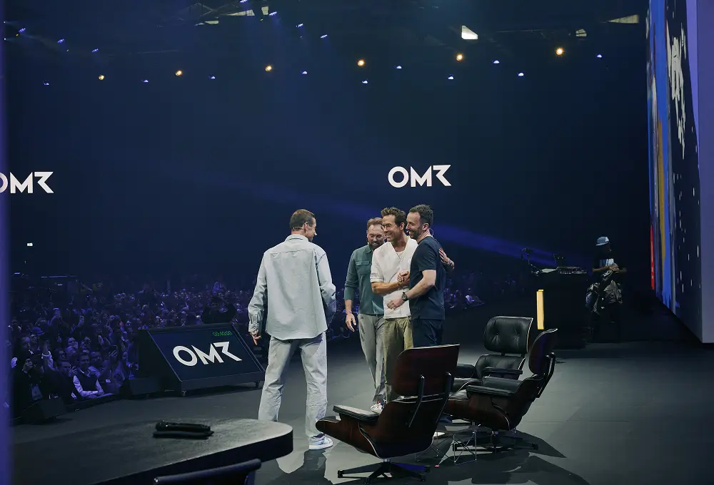 Ryan Reynolds steht mit anderen Teilnehmern auf der Bühne der OMR vor einem großen Publikum, während sie sich unterhalten und die Atmosphäre locker wirkt.