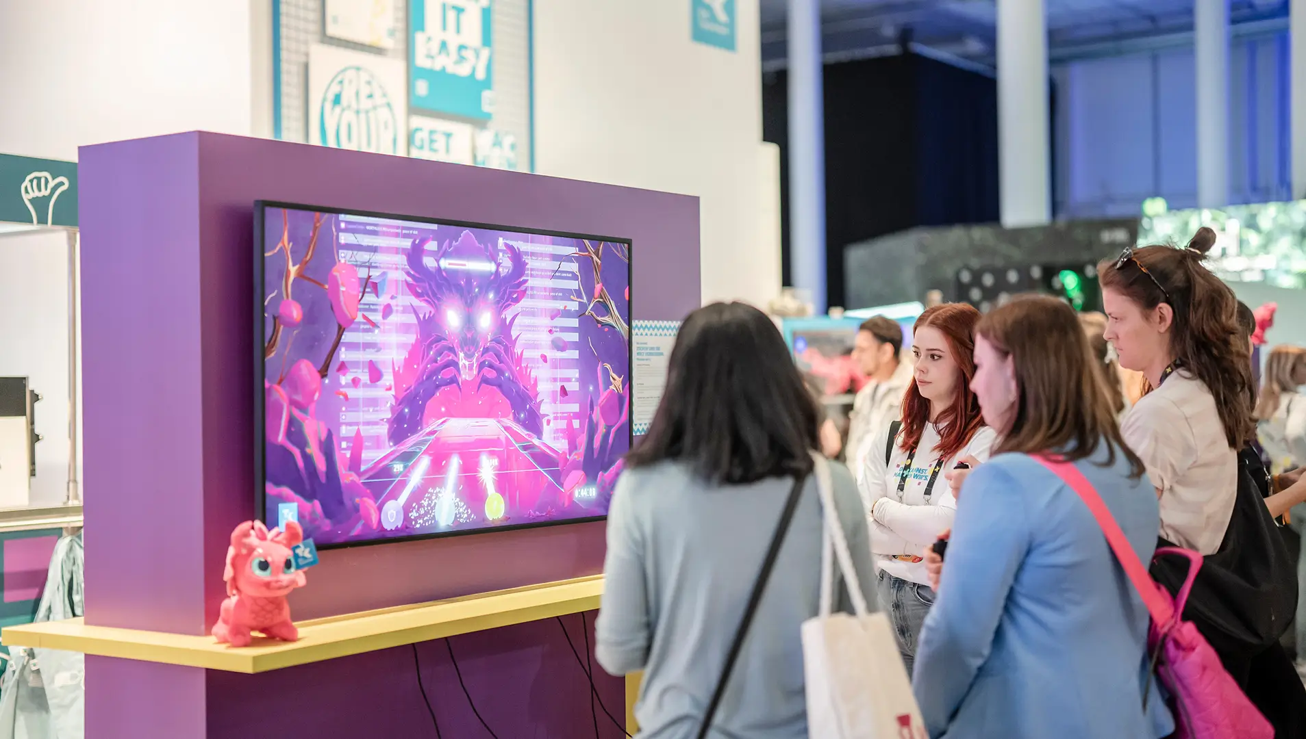 Drei Frauen stehen vor einem Bildschirm am OMR-Stand der Techniker Krankenkasse und spielen ein Spiel gegen das Toxic Monster.