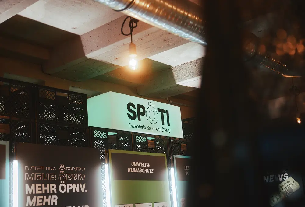 Ein beleuchtetes Schild mit der Aufschrift „SPÖTI – Essentials für mehr ÖPNV“ in einer modernen, industriellen Umgebung.