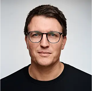Eine Person im Anzug steht vor einem Präsentationsbildschirm mit Text und Grafiken im Hintergrund.
