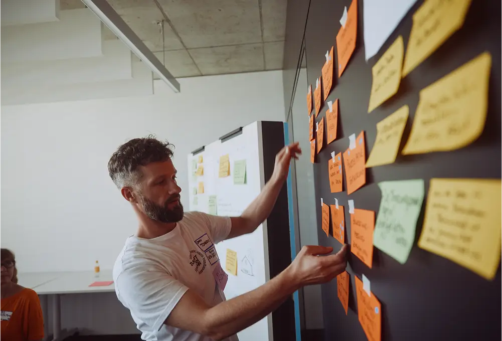 Eine Person befestigt bunte Moderationskarten mit Notizen an einer Wand während eines Workshops.