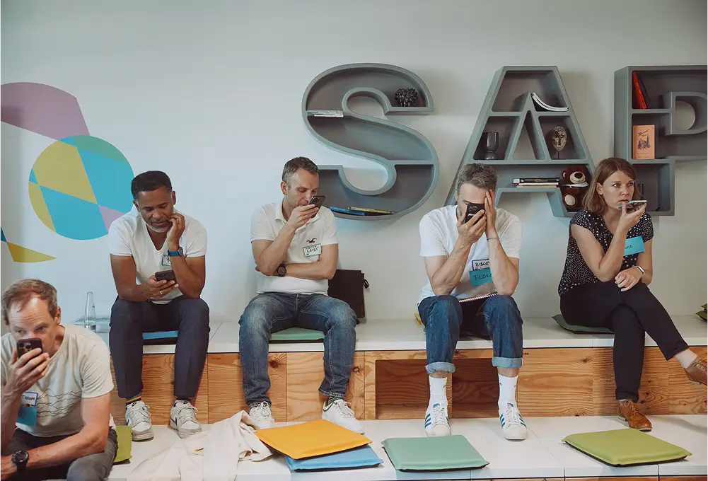 Mehrere Personen sitzen vor einem Regal mit großen SAP-Buchstaben und schauen auf ihre Smartphones.