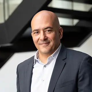 Dr. Ahmed Khalifa steht in einem modernen Gebäude und trägt einen dunklen Anzug mit weißem Hemd.