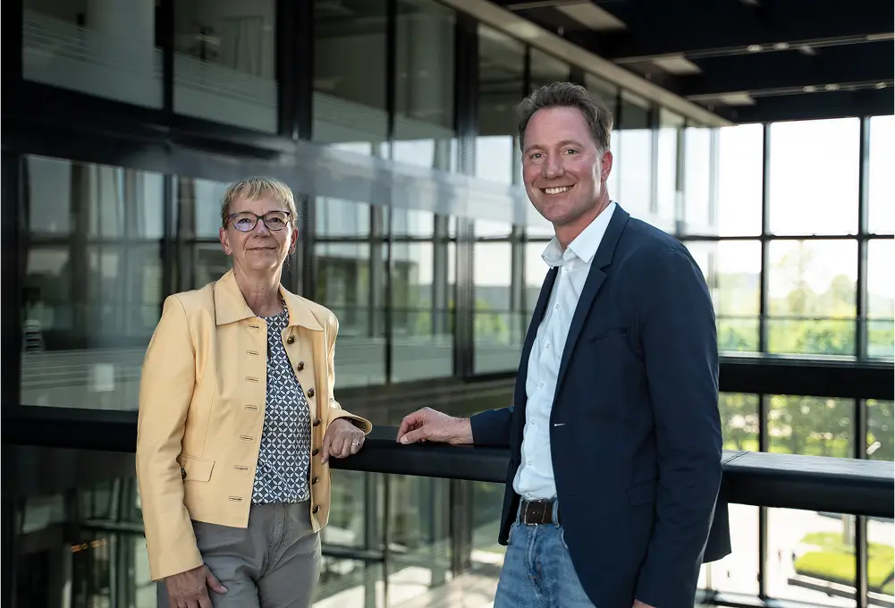 Zwei Personen stehen in einem modernen, lichtdurchfluteten Bürogebäude und unterhalten sich an einem Geländer.