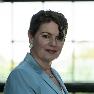 Sigrid Viergutz steht in einem modernen, lichtdurchfluteten Gebäude und trägt einen hellblauen Blazer.