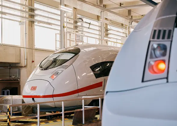 Ein ICE-Zug steht in einer hellen Werkhalle, im Vordergrund ist ein weiterer Zug angeschnitten zu sehen.