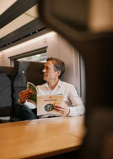 Eine Person sitzt im ICE und liest die Speisekarte des Bordrestaurants.