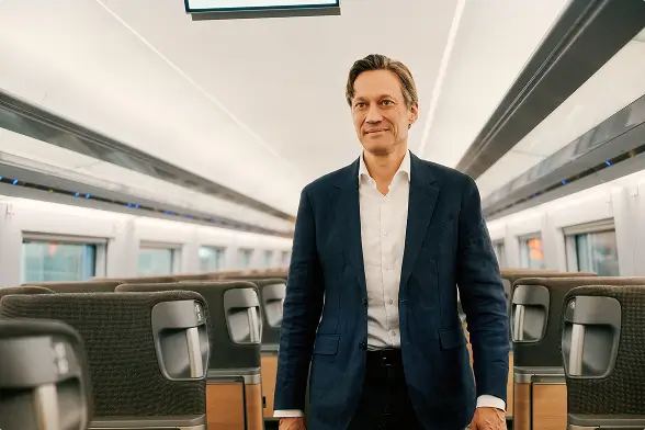 Eine Person im blauen Sakko steht im Mittelgang eines modernen, leeren ICE-Waggons.