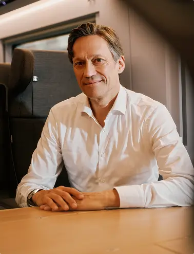 Eine Person sitzt an einem Tisch im ICE und hat die Hände gefaltet vor sich liegen.