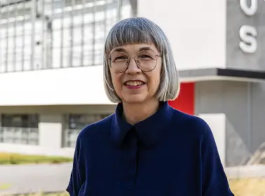 Eine Frau mit grauen Haaren steht vor dem Bauhaus-Gebäude in Dessau.