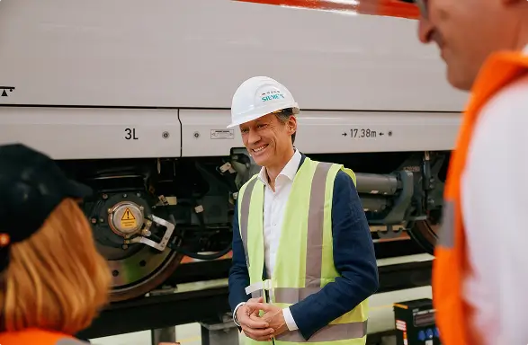 Eine Person mit Schutzweste und Siemens-Helm steht in einer Werkhalle zwischen zwei ICE-Zügen.