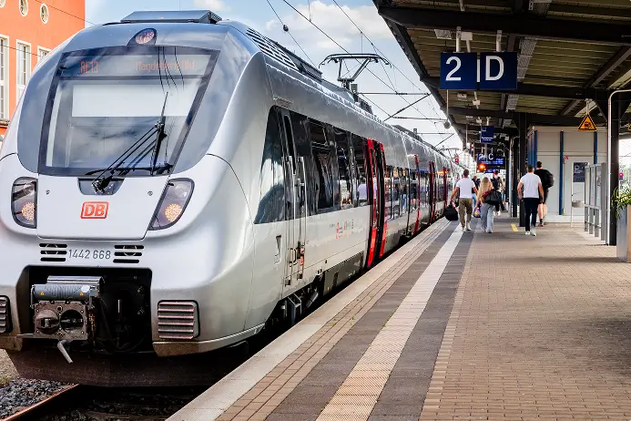 Ein moderner Regionalzug der Deutschen Bahn steht am Bahnsteig, Menschen gehen entlang des Zuges.