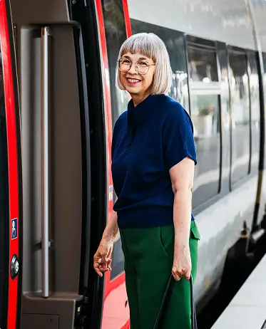 Eine Frau mit weißem Haar steht vor der offenen Zugtür eines Regionalzugs am Bahnsteig.