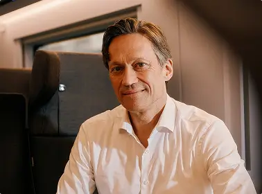 Ein Mann im weißen Hemd sitzt im Abteil eines modernen Zuges.