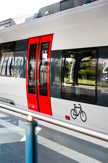 Ein moderner Regionalzug mit roten Türen steht am Bahnsteig, das Fahrrad-Symbol ist zu sehen.