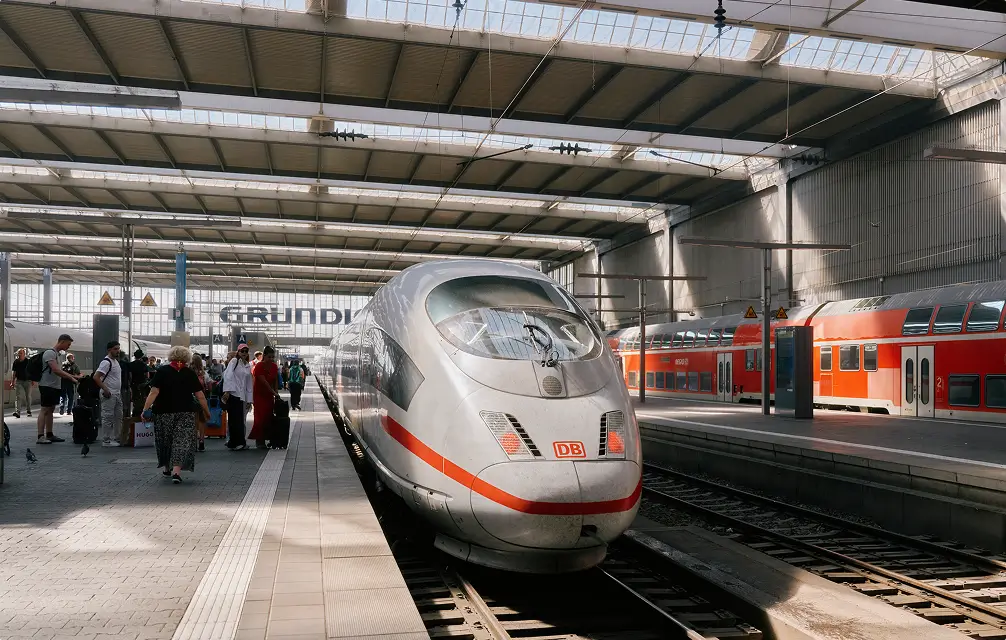 Ein ICE-Zug steht am Bahnsteig in einer Bahnhofshalle, umgeben von Reisenden.