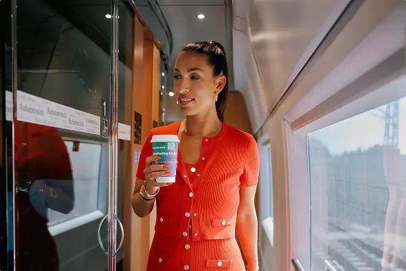 Frau im roten Kleid mit Kaffeebecher im Gang eines Zuges.