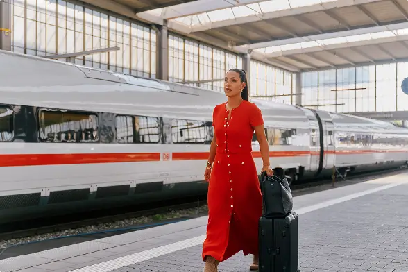 Frau im roten Kleid vor einem ICE-Zug am Bahnsteig.