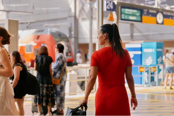 Frau im roten Kleid läuft mit Koffer über einen belebten Bahnsteig.