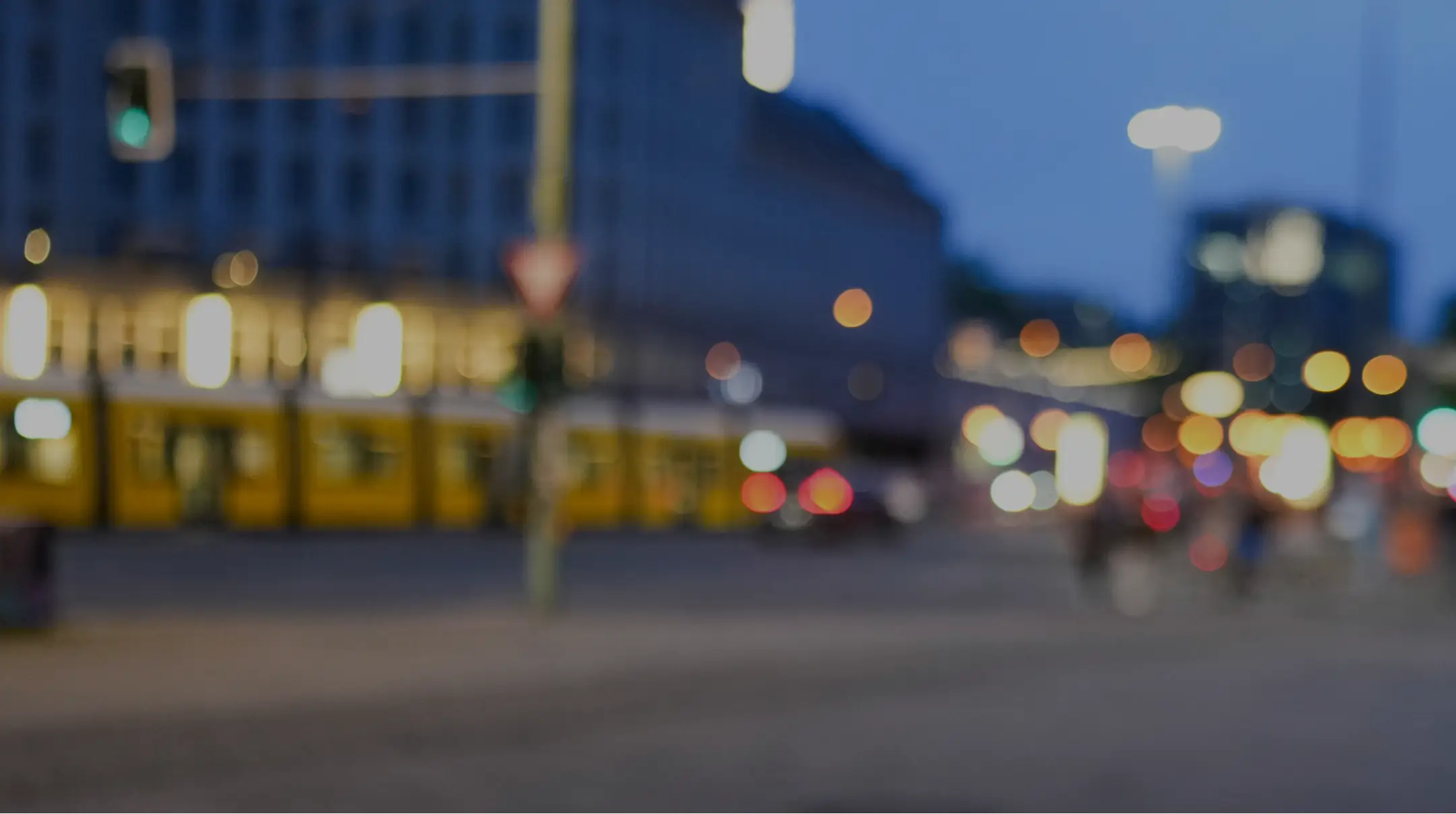 Unscharfe Aufnahme einer nächtlichen Straßenszene mit leuchtenden Straßenlaternen, einem gelben Straßenbahnzug und vorbeifahrenden Autos in der Stadt.