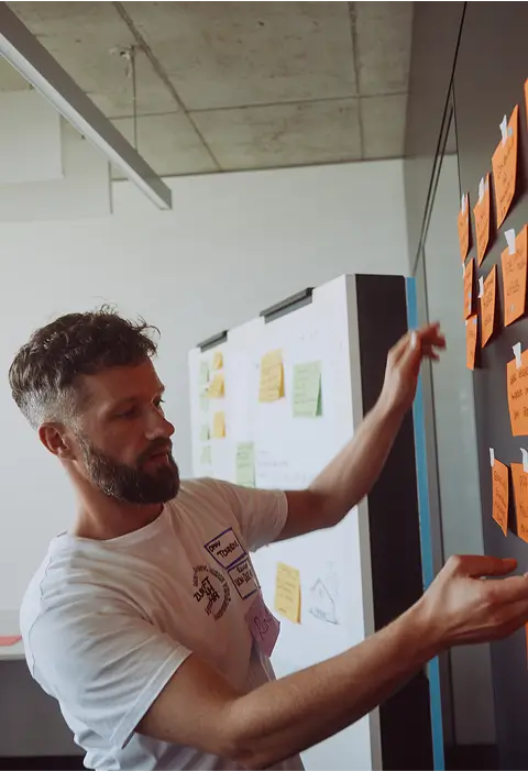 Eine Person befestigt bunte Moderationskarten mit Notizen an einer Wand während eines Workshops.