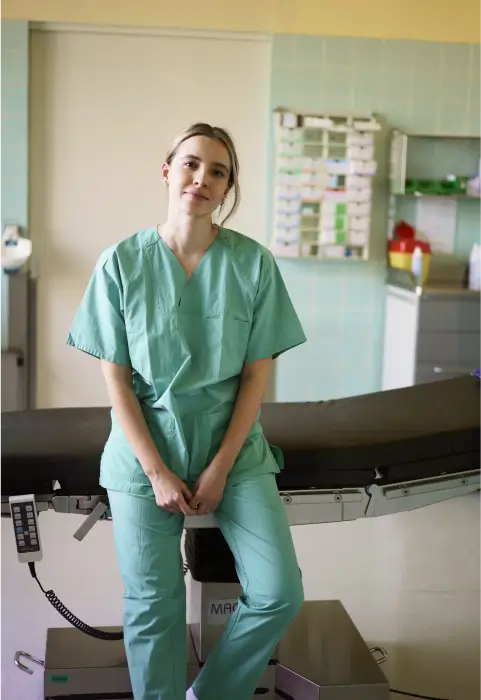 Eine Person in OP-Kleidung sitzt auf einer Liege in einem Krankenhaus- oder Operationssaal.