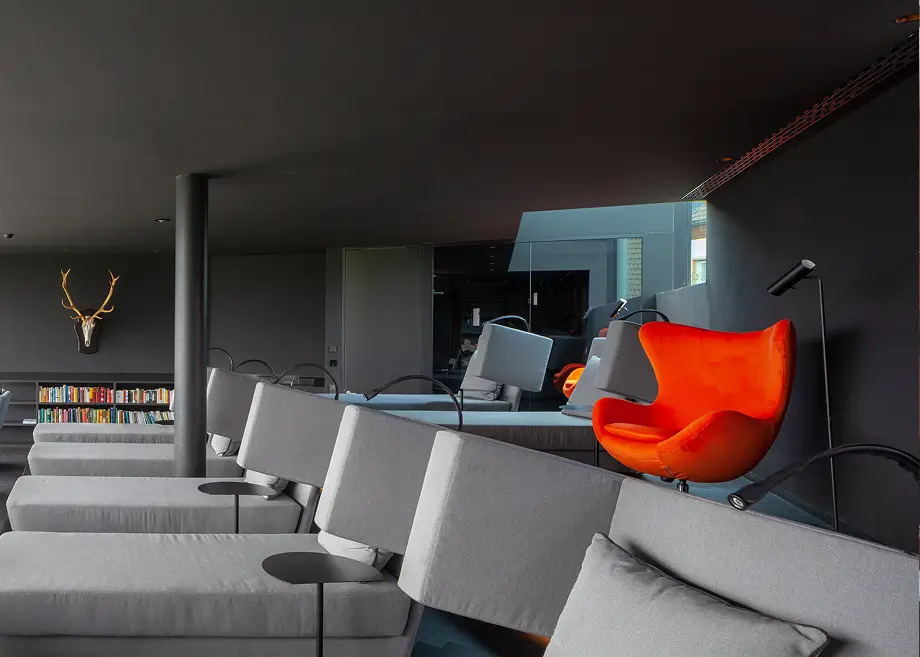 Moderner Wohnraum mit grauen Sofas, orangem Egg Chair und anthrazitfarbener Decke.