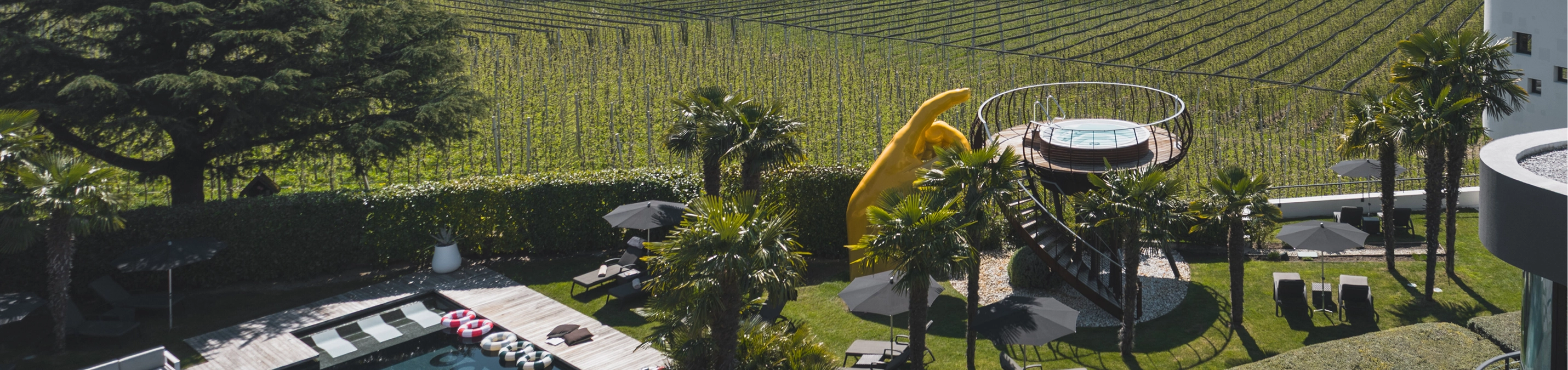 Luxushotel mit Pool, gelber Rutsche und Weinbergen in Südtiroler Berglandschaft.