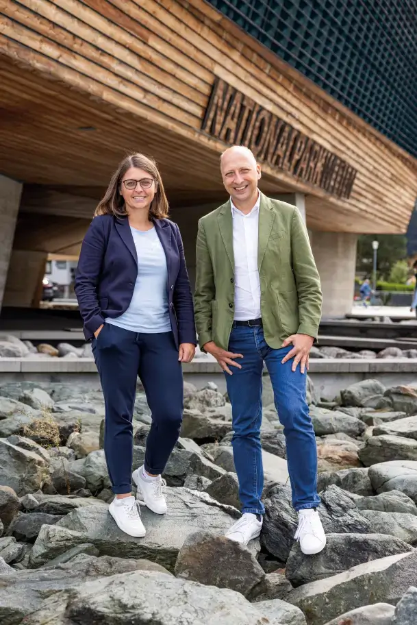 Roland Rauch und Christine Reichholf stehen lächelnd auf Steinen vor dem Gebäude des Nationalparkzentrums Hohe Tauern.
