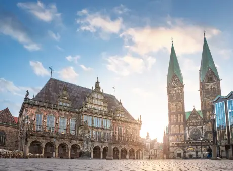 Bremens Marktplatz bei Sonnenschein mit dem Rathaus links und dem Dom mit seinen zwei Türmen rechts.