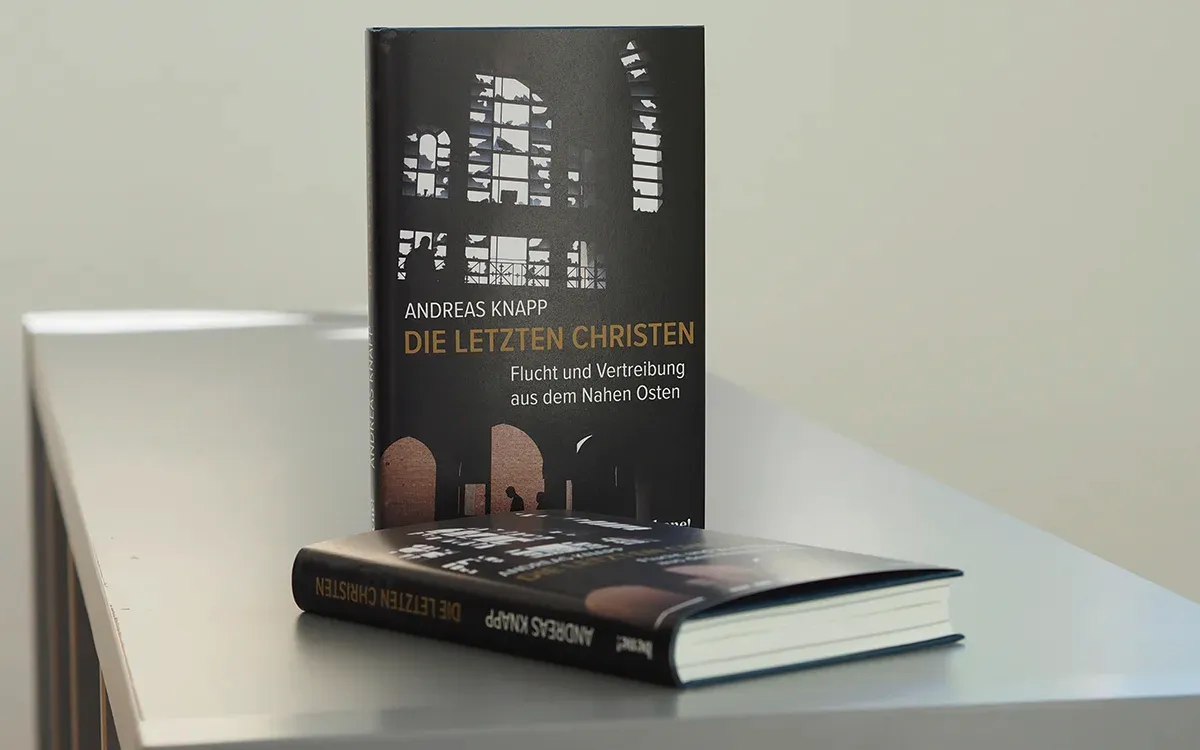 Das Buch „Die letzten Christen“ steht aufrecht auf einem hellen Tisch, während ein zweites Exemplar davor liegt. Auf den schwarzen Umschlägen sind helle Fensterformen und dunkle Torbögen abgebildet.