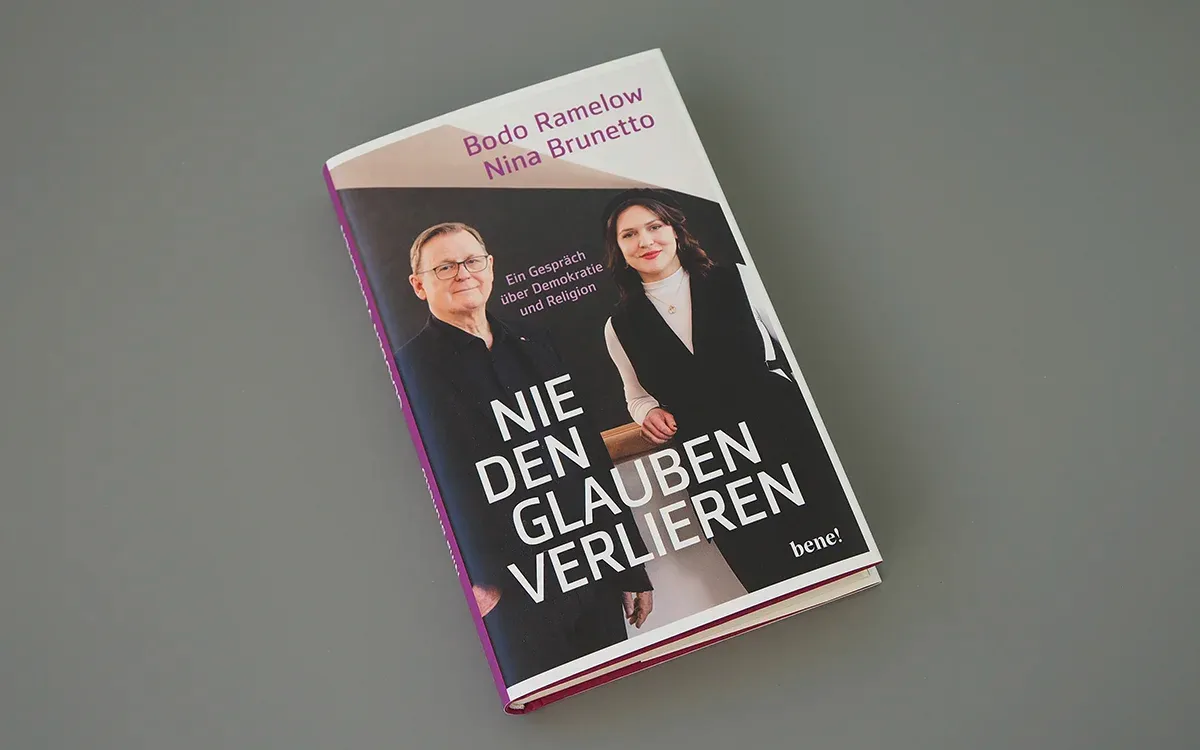Das Buch „Nie den Glauben verlieren“ liegt schräg auf einer grauen Fläche. Auf dem Cover sind ein Mann und eine Frau abgebildet.