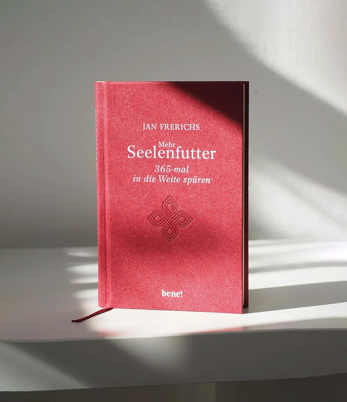 Das rote Buch „Seelenfutter“ steht aufrecht auf einer hellen Fläche. Ein rotes Leseband liegt nach links auf der Fläche.