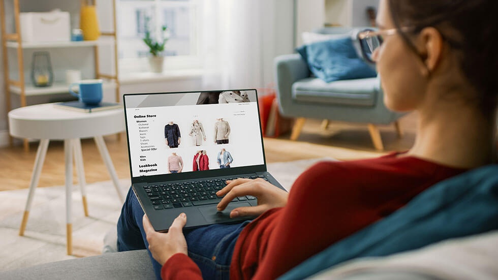 Eine Frau schaut sich auf ihrem Laptop Kleidungsstücke in einem Online Shop an.